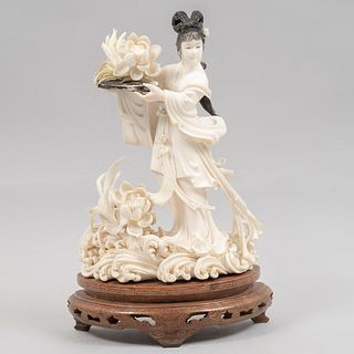 Quan Yin con flor de loto. China, siglo XX. Talla en marfil con detalles en tinta negra y base de madera. 17 cm de altura