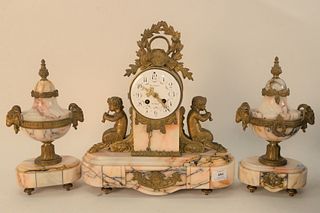 Three Piece Mersmann Clock Set, having marble bases, flanked by two putti figures; glass bezel available, clock height 14 1/2 inches, width 14 1/2 inc
