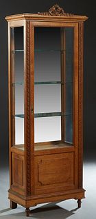 French Louis XVI Style Carved Oak Vitrine, early 20th c., with a pierced ribbon crest, over a center door with a beveled glass upper panel over a fiel