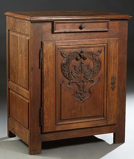 French Provincial Louis XIV Style Carved Oak Confiturier, 19th c., the rounded sloping edge top over a large cupboard door with applied leaf and scrol