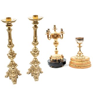 Lote de 4 piezas. Siglo XX. Elaborados en metal dorado. Consta de: Cáliz con base de madera, candelabro y par de portacircios.