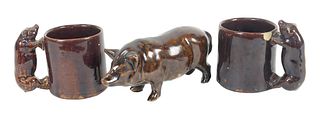 Three Brown Glazed Pottery Pieces, to include standing pig, height 4 inches; along with a pair of mugs with pig form handles, height 3 inches. Provena