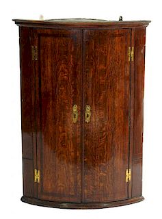 A GEORGE III OAK AND CROSSBANDED BOW FRONTED CORNER CUPBOARD