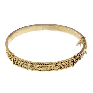 A late 19th century gold hinged bangle. The beaded motif, to the rope-twist border and scrolling sid