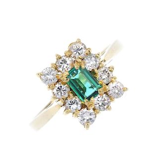 An 18ct gold emerald and diamond cluster ring. The rectangular-shape emerald, within a brilliant-cut