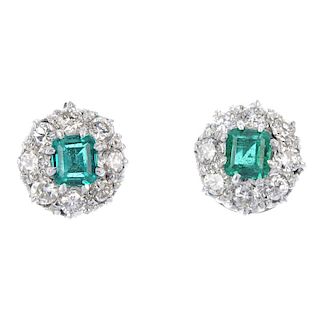 A pair of emerald and diamond cluster ear studs. Each designed as a square-shape emerald, within a b
