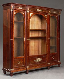 French Empire Ormolu Mounted Carved Mahogany Bookcase, early 19th c., the stepped breakfront crown over an arched center door with a glazed upper pane