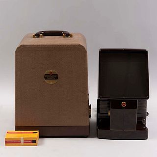 Proyector de mesa. E.U.A. SXX. De la marca Kodak Slide 4x. Elaborado en baquelita y material sintético. Con lente regulable y estuche.