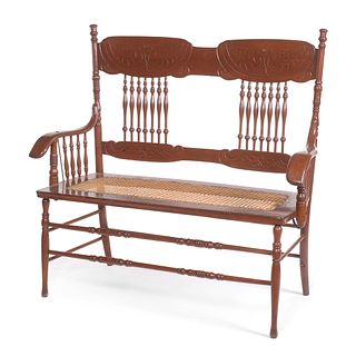 Love seat. SXX. Estilo Early American. Elaborado en madera tallada. Respaldo con barandillas, asiento de bejuco.