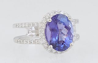 Lady's Platinum Dinner Ring, with an oval 4.12 ct. tanzanite atop a conforming border of round diamonds, the split shoulders of the band also mounted 