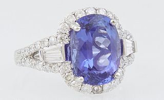 Lady's Platinum Dinner Ring, with an oval 4.45 ct. tanzanite atop a conforming border of round diamonds, with diamond baguette mounted lugs, the split