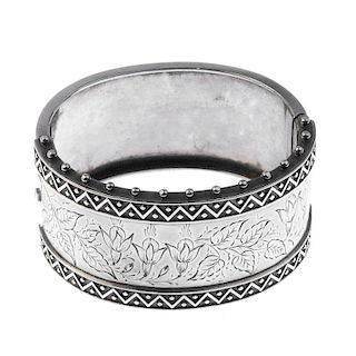 A late 19th century silver bangle, the front designed as a floral engraved panel, flanked by a geome