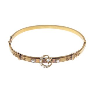 An early 20th century gold and split pearl bangle. The hinged, slim, gold bangle with applied bead a