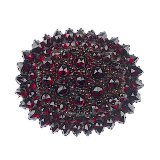 A memorial garnet brooch. Of oval outline, the circular garnets of varying sizes set to a tiered mou