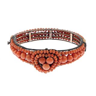 A coral bangle. Designed as a central heart-shape openwork panel set with three circular coral caboc