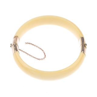 An early 20th century ivory and 9ct gold bangle. The hinged ivory bangle with gold terminals and cla