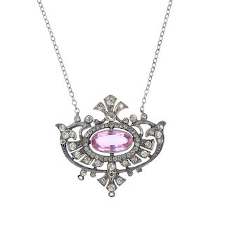 A paste pendant. The central oval-shape pink paste within a scrolling openwork surround set with col