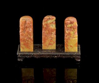 Set of three Chinese orange/green soapstone carvings of immortals on square bases on rectangular bas