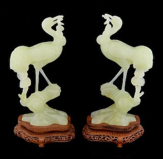 Pair of carved green jadeite cranes each with a branch in it's mouth, on hardwood bases, 24cm high,