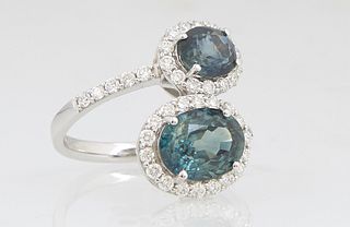 Lady's 18K White Gold Dinner Ring, the bypass band terminating in two prong set oval natural green sapphires, atop conforming borders of tiny round di
