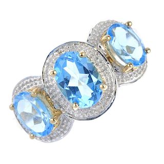 A 9ct gold topaz and diamond dress ring. The three graduated oval-shape blue topaz, each within a si