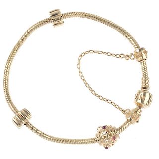 PANDORA - a 14ct gold charm bracelet. The spiral-link bracelet, with a series of four charms, to inc