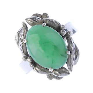 A jadeite dress ring. The oval jadeite cabochon, within a foliate surround, to the plain band. Weigh