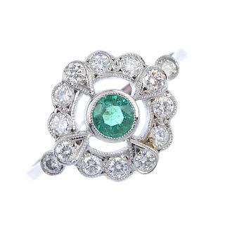 An emerald and diamond dress ring. The circular-shape emerald collet, within a brilliant-cut diamond