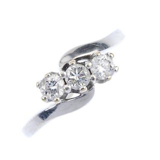 An 18ct gold diamond three-stone crossover ring. The brilliant-cut diamonds, to the asymmetric shoul