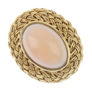 A coral single-stone ring. The oval coral cabochon, within an interlinked border, to the plain band.