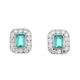 A pair of emerald and diamond ear studs. Each designed as a rectangular-shape emerald, within a bril