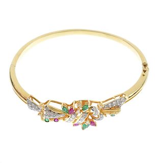 A diamond, ruby and emerald hinged bangle. The front designed as a textured, scrolling panel, set th
