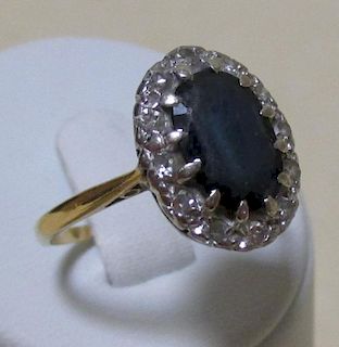 A sapphire and diamond cluster ring, the oval dark blue sapphire claw set in a border of round brill