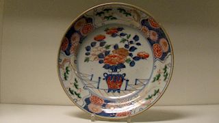An early 18th century Imari plate, centrally painted with a vase of flowers on a fenced terrace with