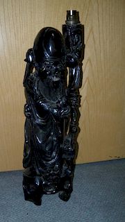 A hardwood carving of Shoulao as a lamp, he stands on a tripod base holding a peach in his right han
