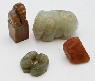 Four Piece Group
to include two carved jade figures, elephant with boy carved from russet celadon jade, a double foo dog figure, along with two soapst