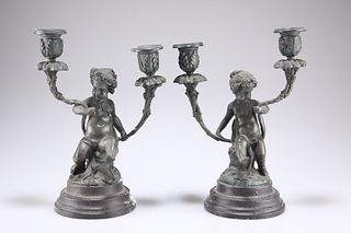 A PAIR OF BRONZE TWO-LIGHT CANDELABRA, each modelled as a putto sitting on 