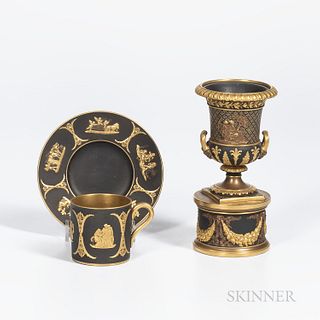 Two Wedgwood Gilded Black Basalt Items, England, c. 1885, a coffee can and saucer with classical figures within scrolled foliate frames, saucer dia. 4