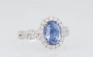 Lady's 18K White Gold Dinner Ring, with an oval 2.25 carat blue sapphire atop a border of round diamonds, the twisted split shoulders of the band also