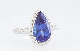 Lady's 18K White Gold Dinner Ring, with a 4.09 ct. pear shaped tanzanite atop a conforming border of round diamonds, the shoulders of the band also mo