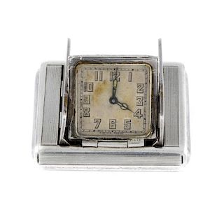 A travel clock. Silver case. Manual wind movement. Discoloured dial with Arabic numeral hour markers