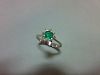 An emerald and diamond ring, set with a round cut emerald in a small petal border of eight single cu