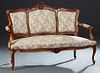 French Louis XV Style Carved Walnut Settee, early 20th c., the arched C-scroll and floral carved crest rail, over three upholstered panels, within uph