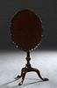 English Carved Mahogany Oval Tilt Top Table, c. 1900, the dished serpentine edge top on an urn form support, to tripodal cabriole legs with pad feet, 