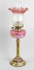 A brass paraffin lamp. The flaring glass shade having frilled rim fading from pink to opaque, raised