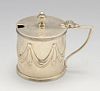 An Edwardian silver mustard pot, the drum form embossed with swags within reeded borders, hinged cre