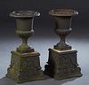 Pair of Campana Form Cast Iron Garden Urns, with relief oval medallion rims over ribbed sides to a socle support on a square base, with iron plinths w