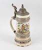 A German porcelain stein, decorated with drinking scene between raised foliate borders and lobed bas