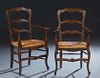 Pair of French Provincial Carved Oak Rushseat Armchairs, 20th c., the arched canted ladderback over curved scrolled arms, to a bowed woven rushseat, o