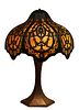 Unusual American Art Nouveau Patinated Spelter Table Lamp, c. 1920, the bulbous circular brass floral cutout shade with caramel slag glass panels, one